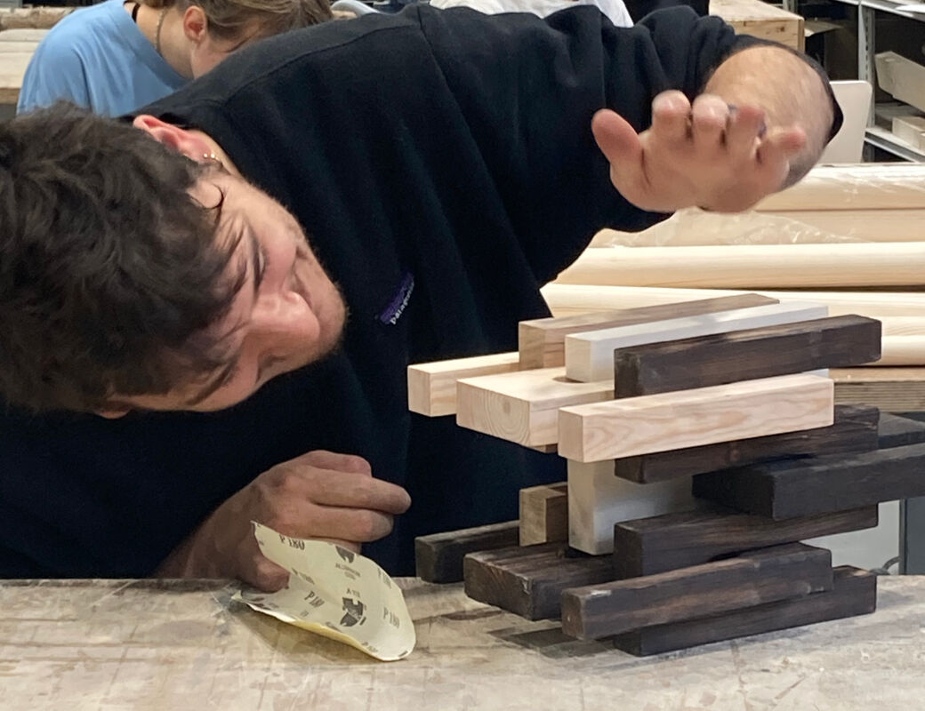 Student working on wooden pieces at a table in workshop