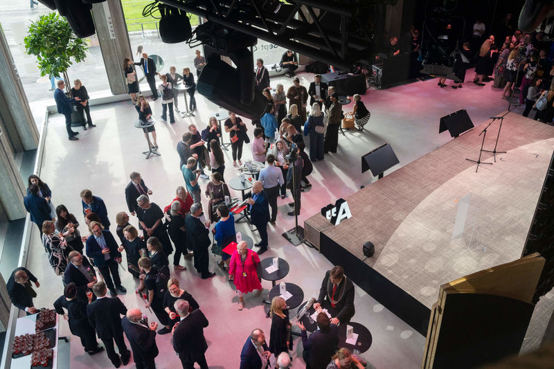 Aerial view of people socialising in a modern event space with high ceilings and large windows.