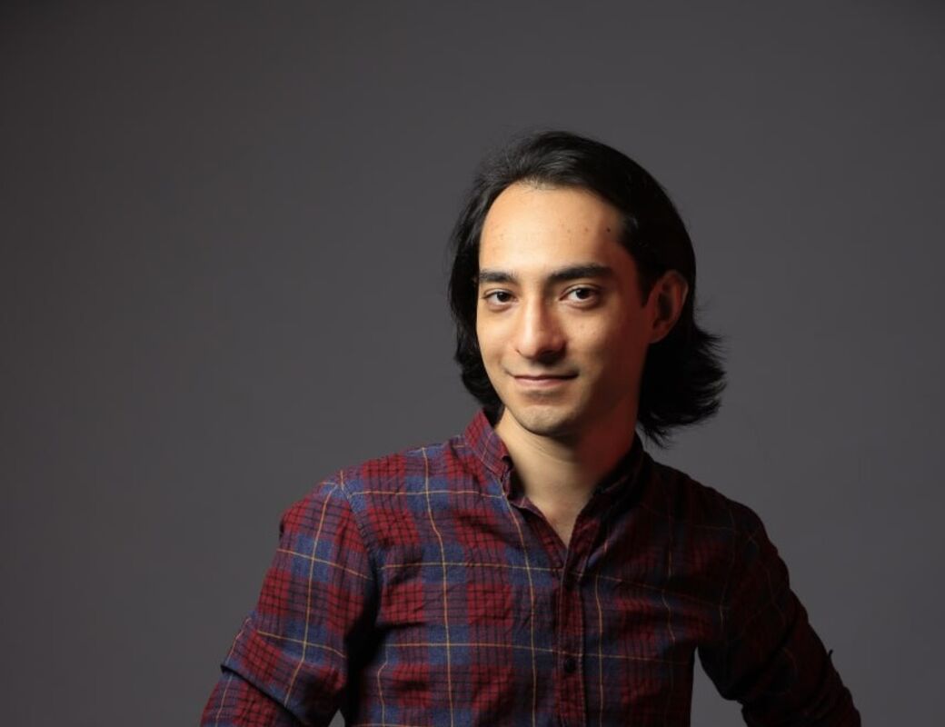 In the grey background, a close-up of a person with dark hair and a blue-red checkered shirt.