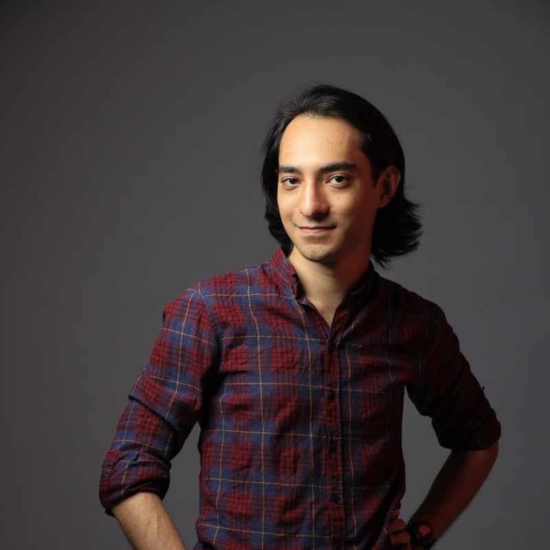 Harmaalla taustalla lähikuva henkilöstä, jolla on tummat hiukset ja sini-punainen ruutupaita.