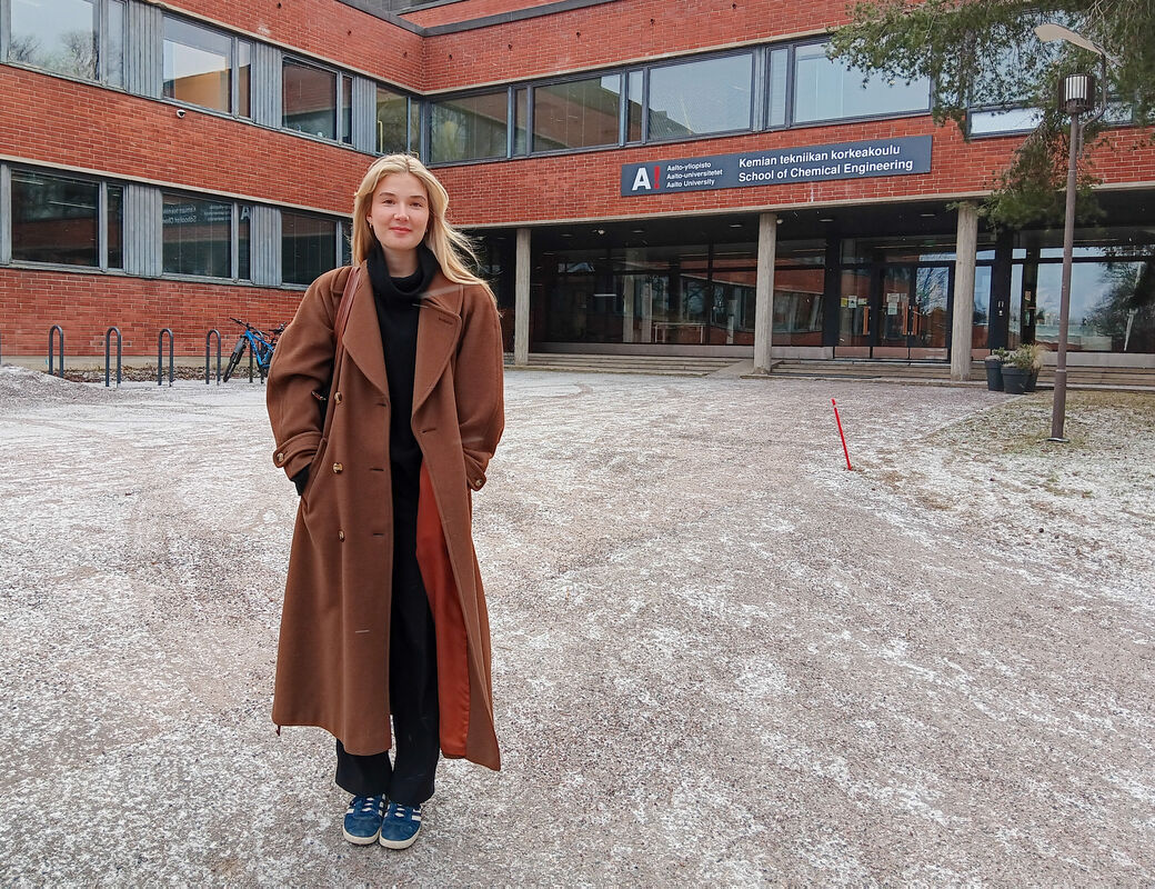 En person i en lång brun kappa står framför en byggnad med skylten 'School of Chemical Engineering'.