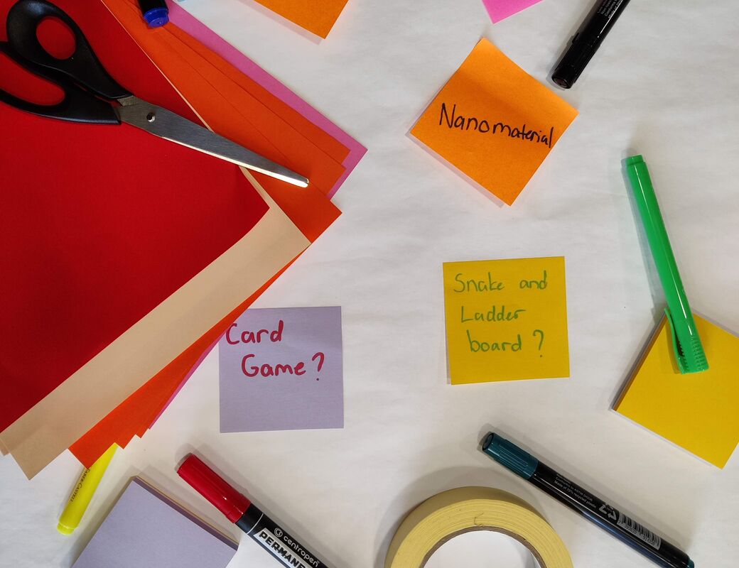 A table with red paper, sticky notes, markers, scissors and tape, featuring words like 'Sustainability' and 'Nanomaterial'.