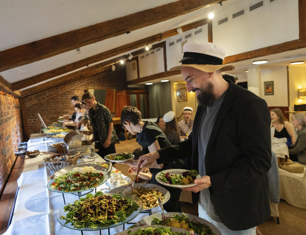 People in casual attire enjoy an indoor buffet. The room has exposed beams and brick walls.
