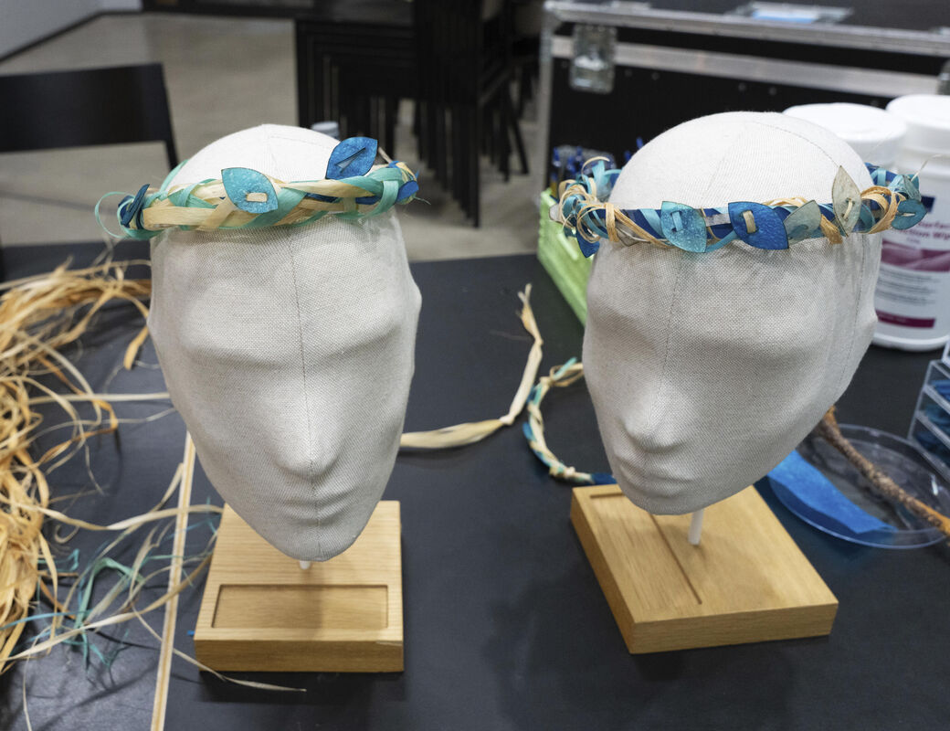 Two head mannequins with handmade wreaths of dried plants and blue paper leaves on a table.