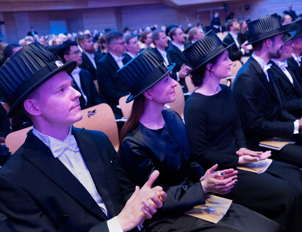 People wearing academic caps and formal attire seated at an indoor event.