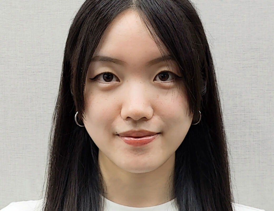 Person with long, straight, dark brown hair wearing a white top and silver hoop earrings.