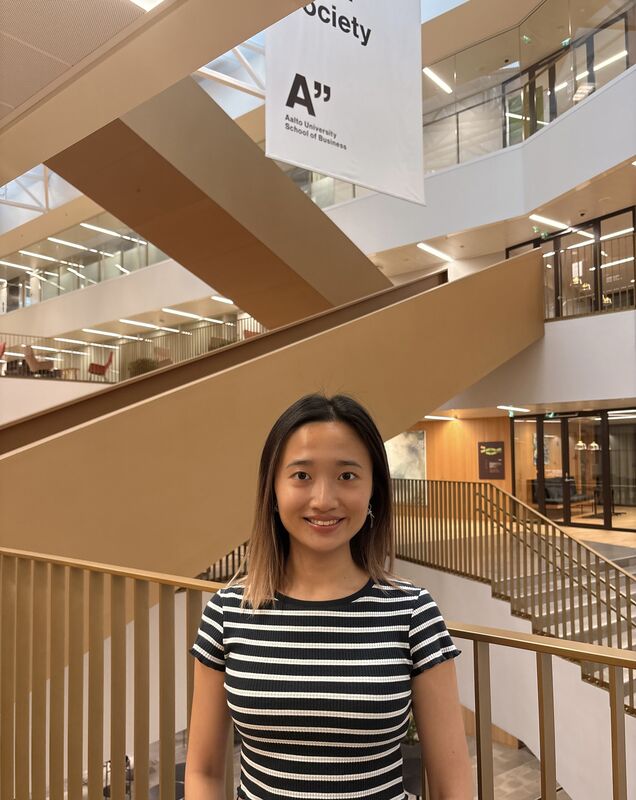 Woman in a black and white striped shirt standing in a modern building of Aalto University School of Business.