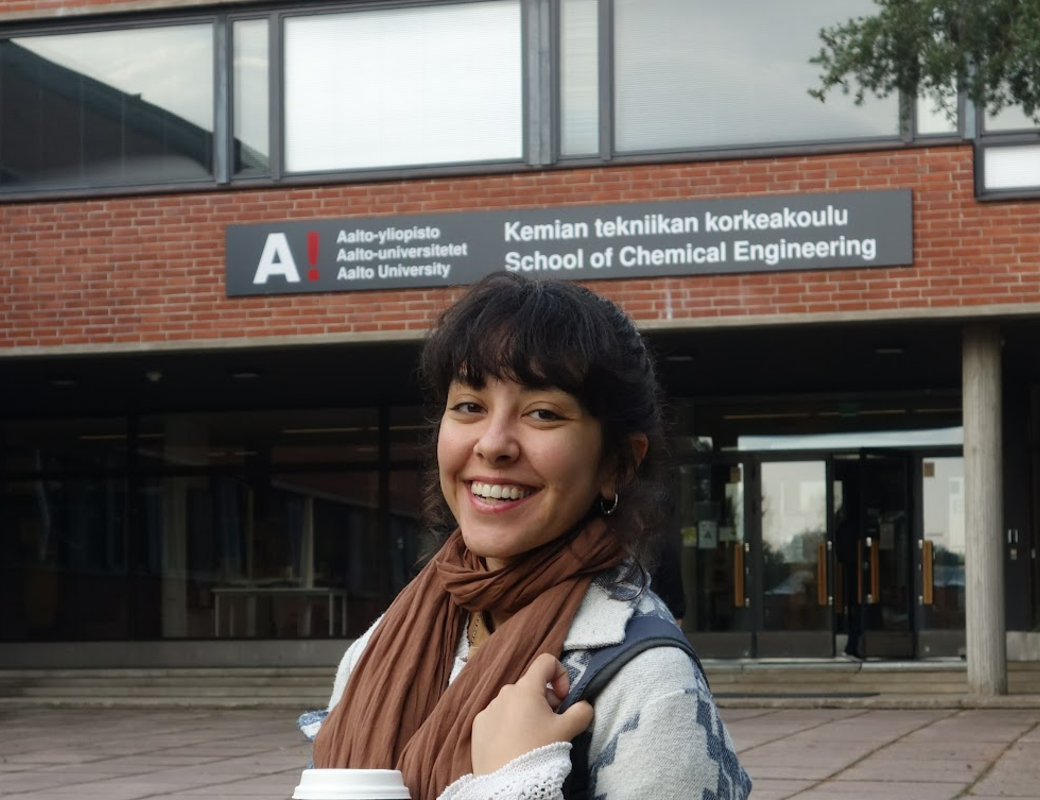 Person håller en kopp står framför Aalto universitetets byggnad för kemiteknik.