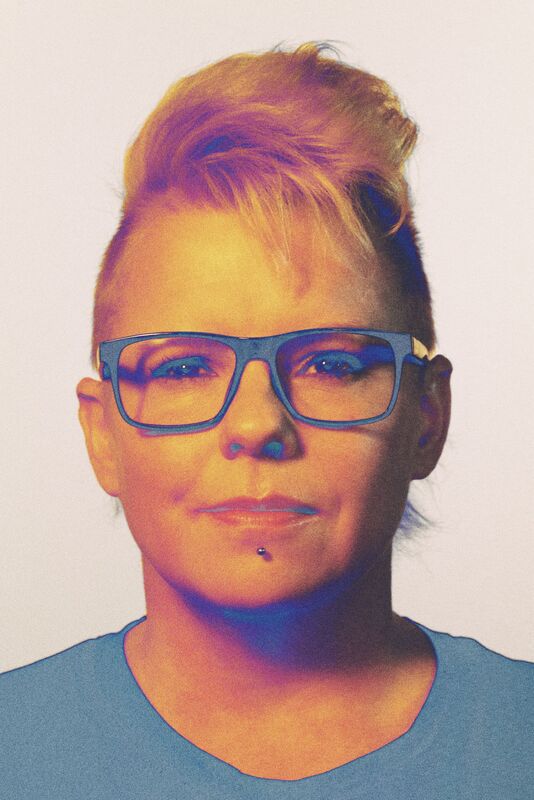 Person med kort, stylat hår som bär glasögon och en blå tröja.