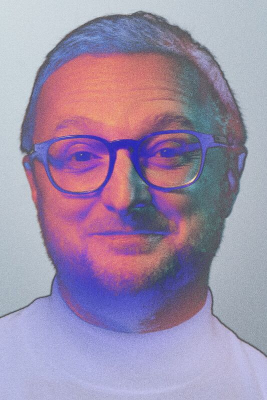 En person med kort hår som bär en vit skjorta mot en grå bakgrund.