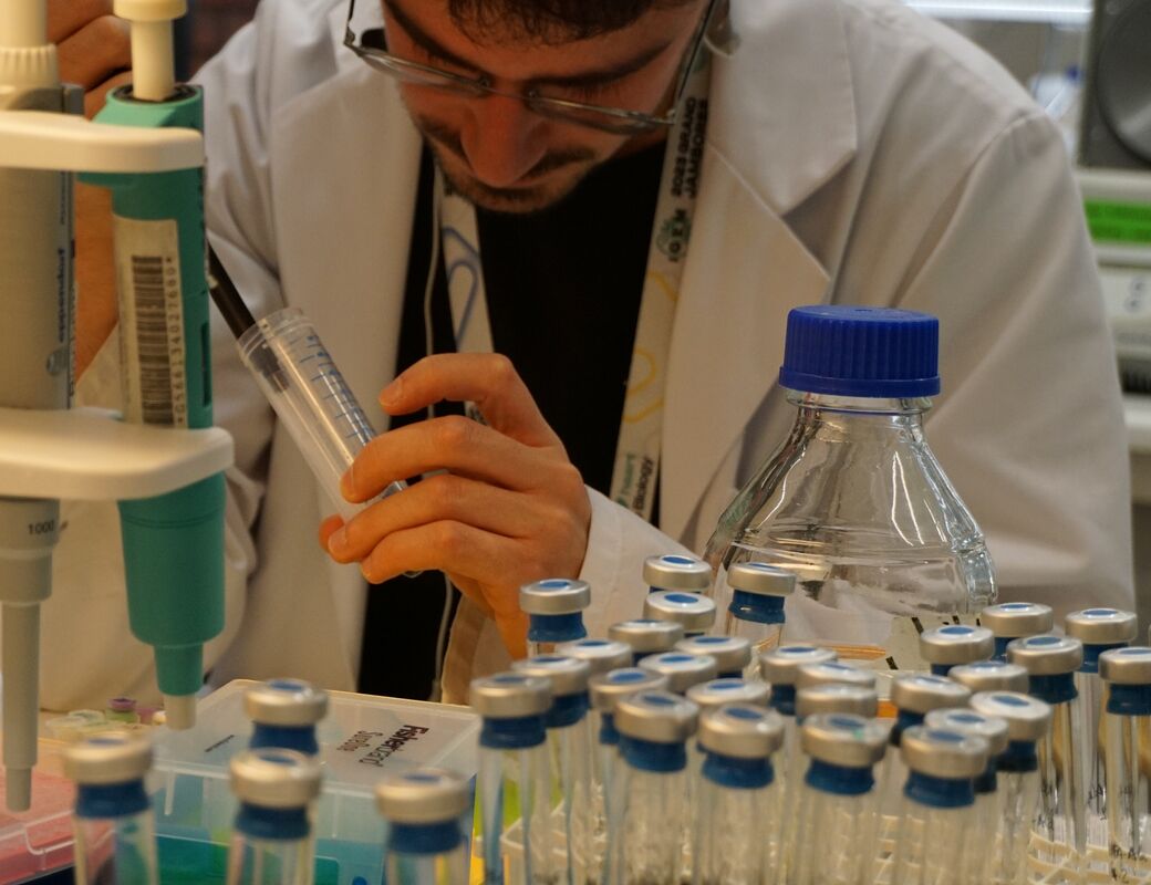 Laboratoriearbetare i vit rock använder spruta bland stativ med provrör och flaskor
