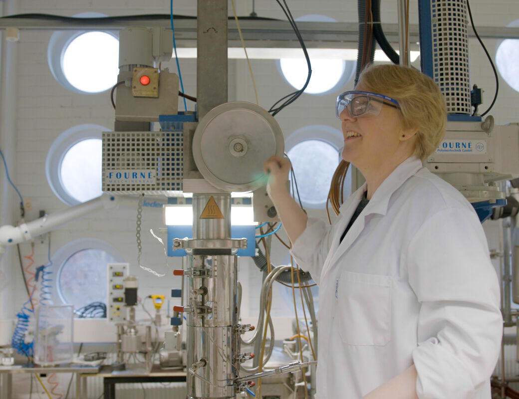 Person in white lab coat operating tall industrial machine in bright laboratory with round windows