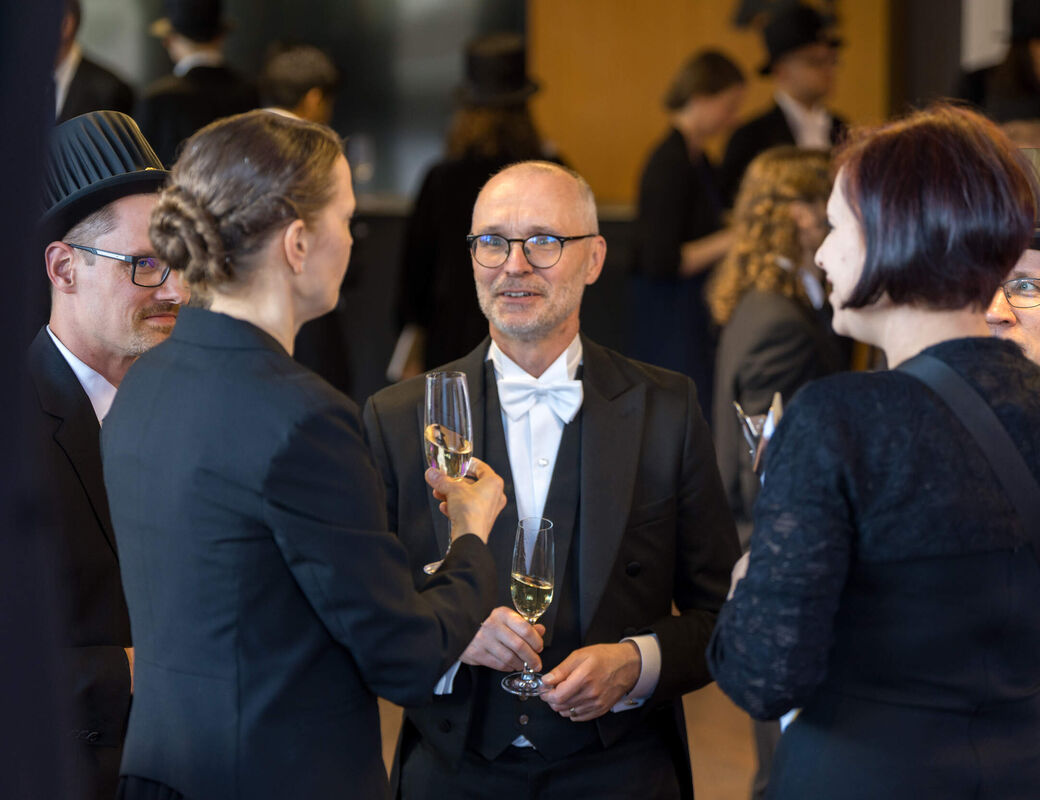 People in formal black suits and top hats chatting and holding champagne glasses at a reception