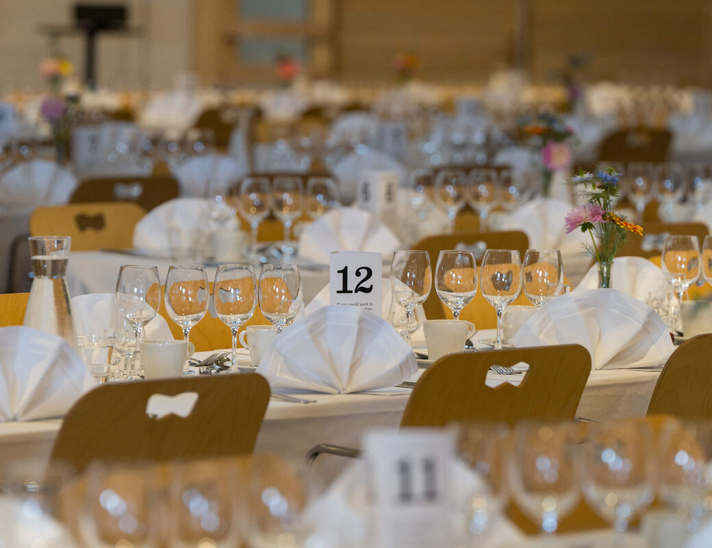 Elegant banquet hall with white table settings, glasses, flowers and table number 12 in focus