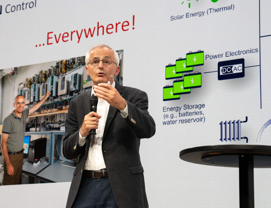 Speaker with microphone presenting an energy systems slide showing solar, batteries and lab photo