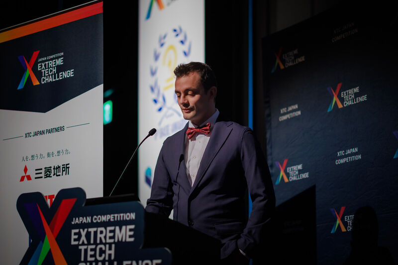 Male speaker in dark suit and red bow tie at Extreme Tech Challenge Japan podium