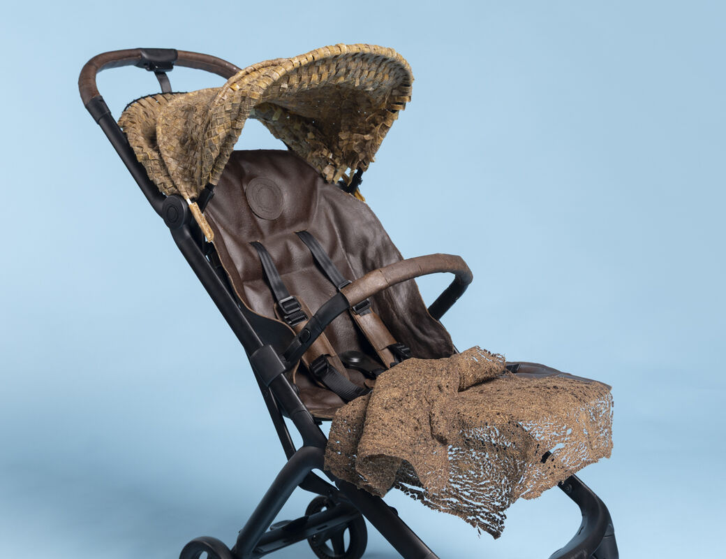 Brown and black pushchair with a woven canopy and rough fabric seat, on a light blue studio background.