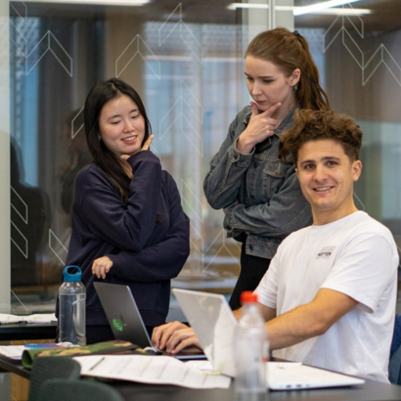 Three students posing with laptops and study material.