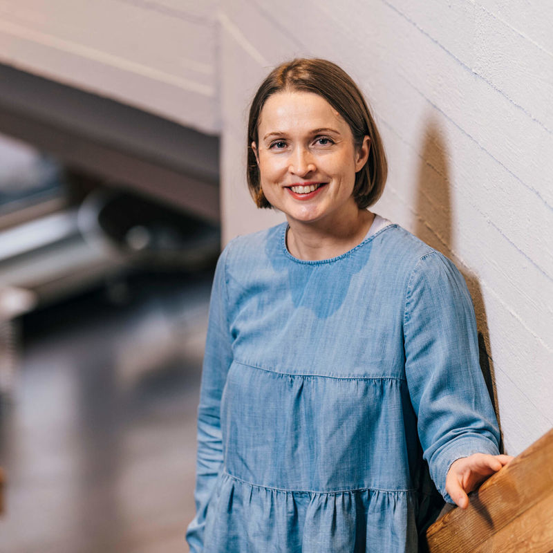 Professori Paula Jouhten nojaa kaiteeseen ja hymyilee kameralle.