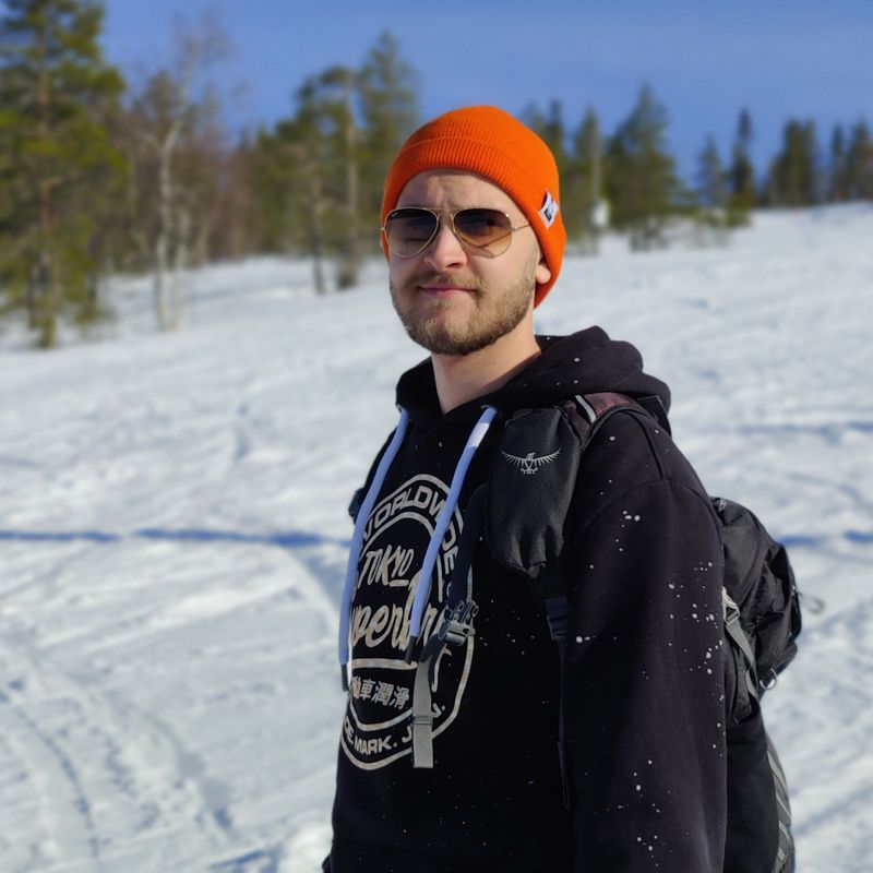 Akseli Rautakorpi kuvattuna lumisessa metsämaisemassa, aurinkolasit päässä.