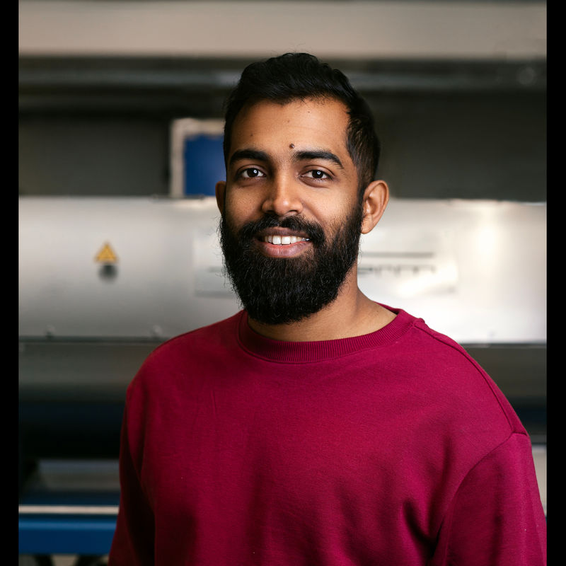 A portrait of Madhawa Basnayaka wearing a red sweater.