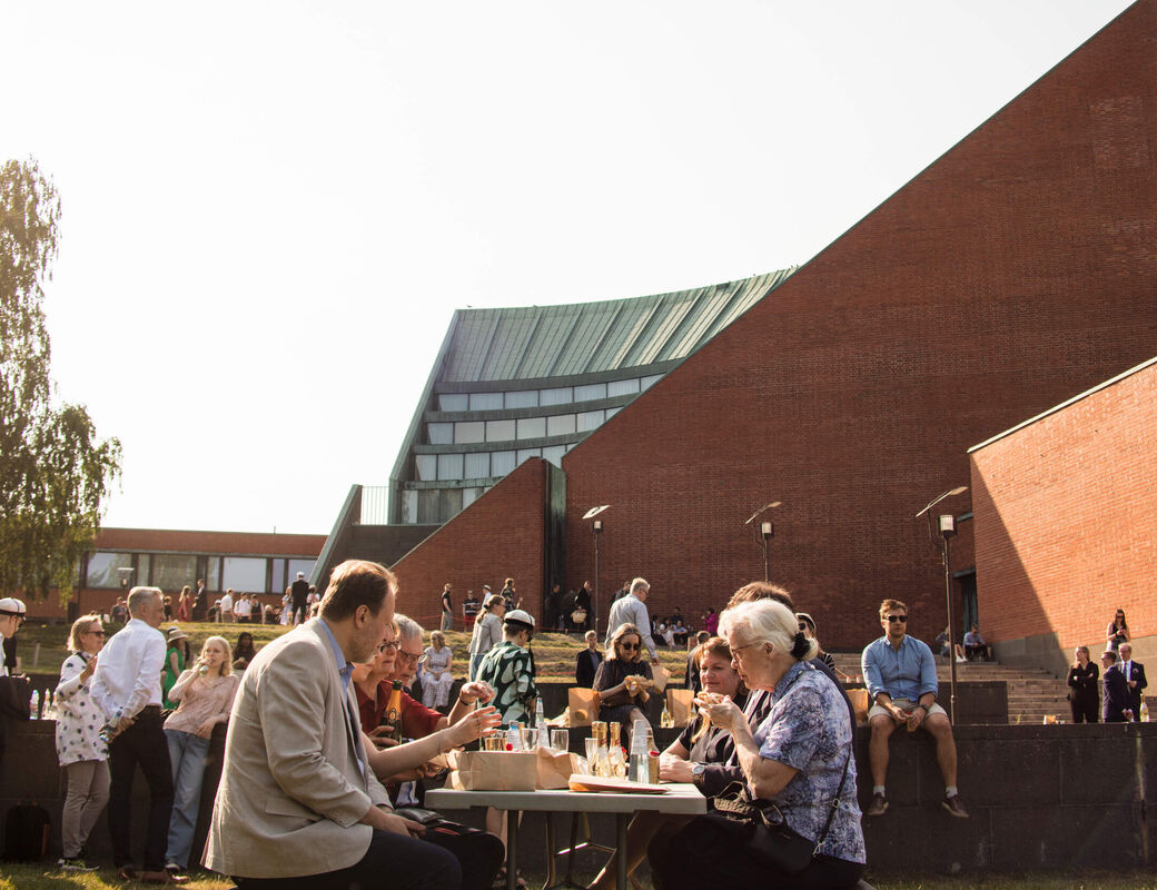 People sitting outside around a table in front of the Otaniemi main building