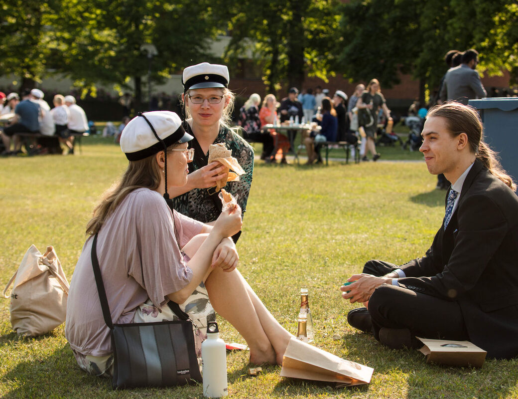 Three graduates sitting and having a picnic at the park