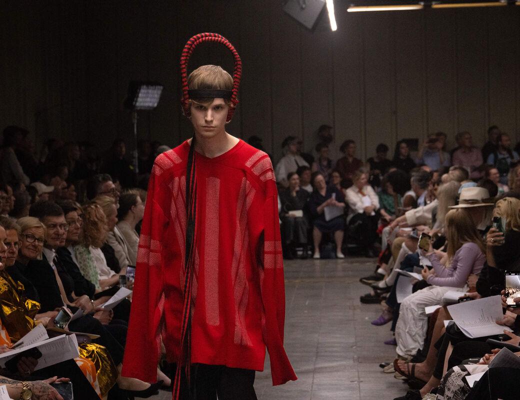 Model walks the catwalk in red outfit and red headpiece