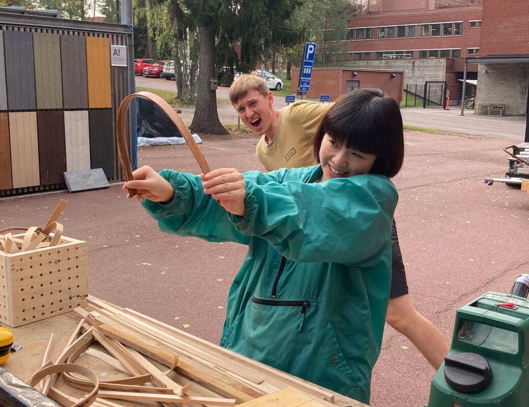 Two students watching tensely as one of them bends a piece of wood to near breaking point