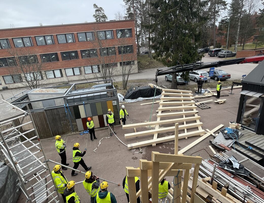 The truss lying on the ground waiting to be lifted, students standing around wearing safety gear