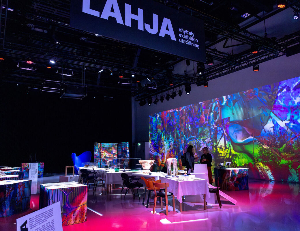 Modern exhibition room with colourful abstract projections on the walls and various artworks on display.