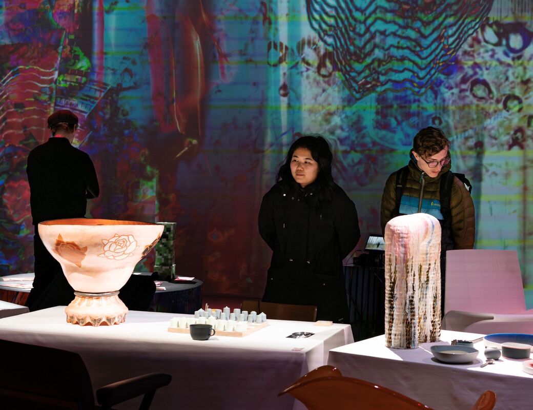 An exhibition room with abstract, colourful projections on the walls and various objects displayed on tables.