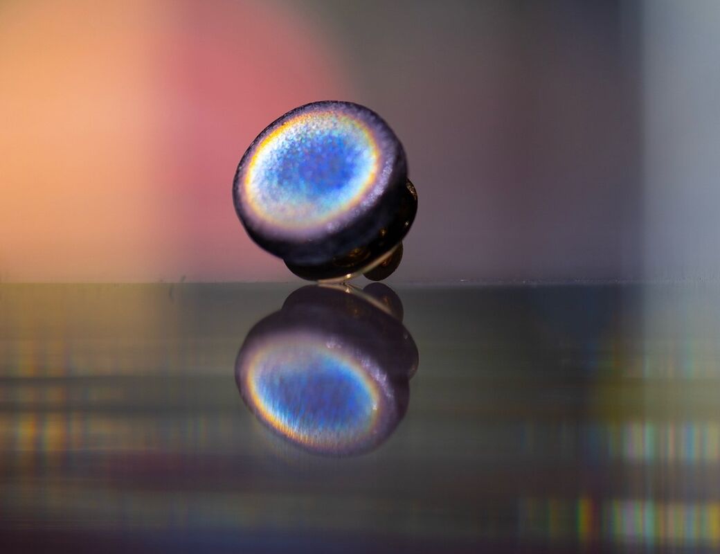 Close-up of a iridescent, round campaign pin reflecting on a shiny surface with a blurred colourful background.