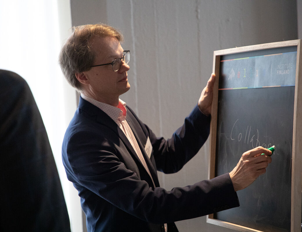 A man holding a chalkboard and writing with a green chalk. A glass of champagne is next to him.