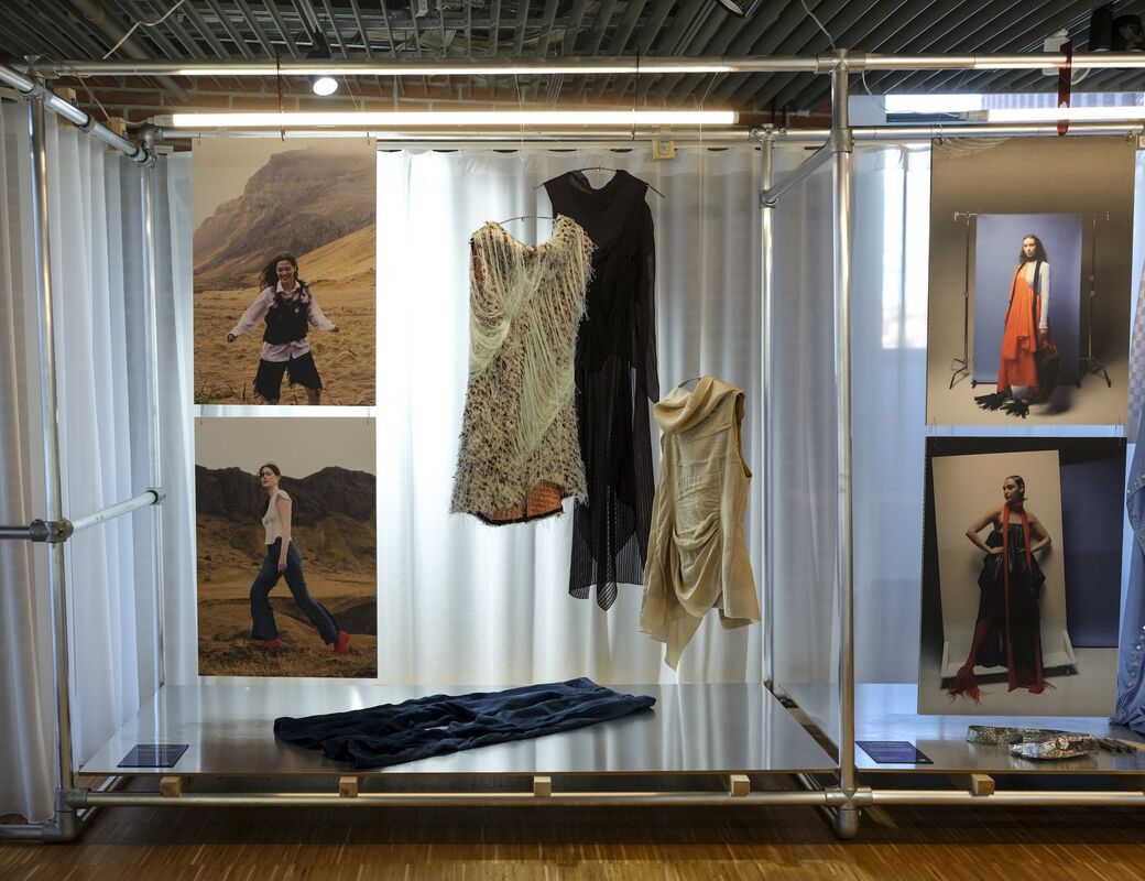 A display of fashion items includes photos, hanging garments, and draped fabric. Clothes feature beige, black, and red details.