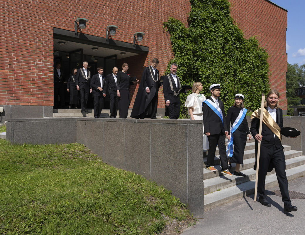 A group of people in formal attire walking down steps outside a brick building with green ivy.