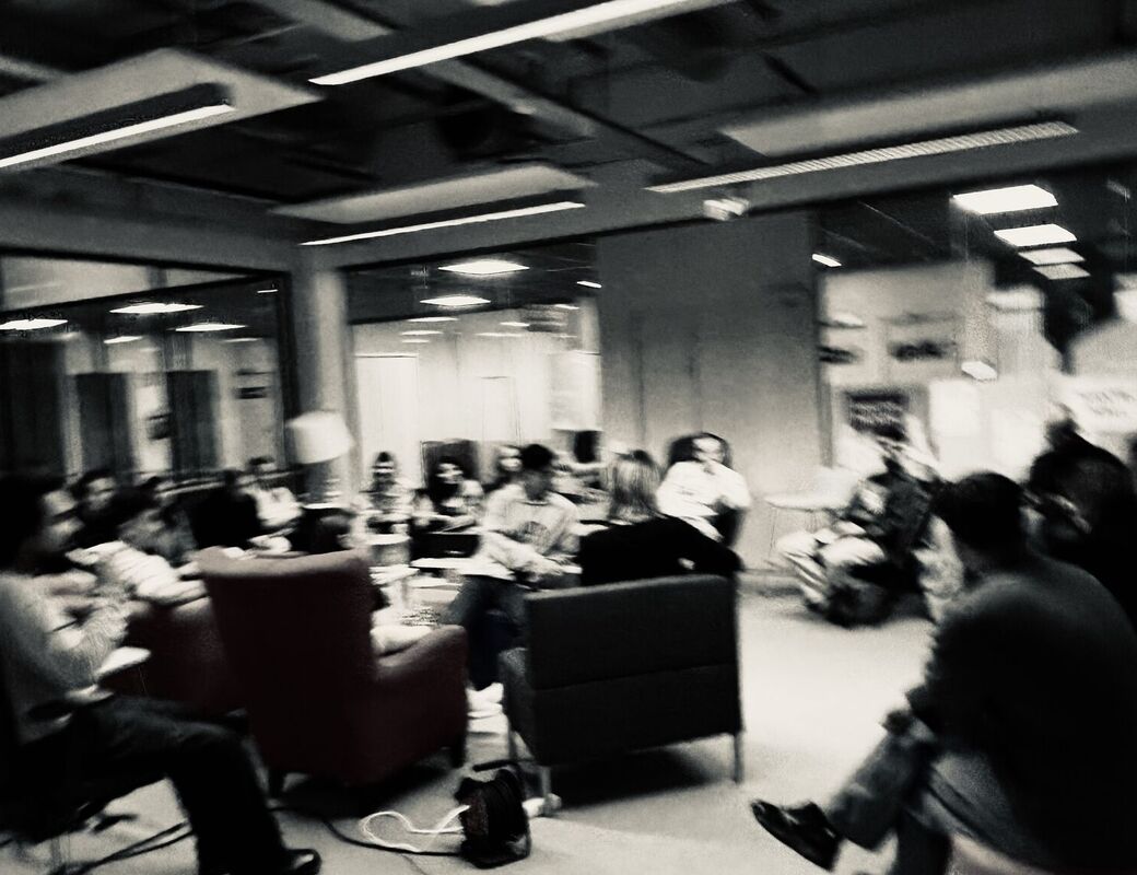 A blurred image of a group of people sitting and discussing in a modern office space with glass walls.