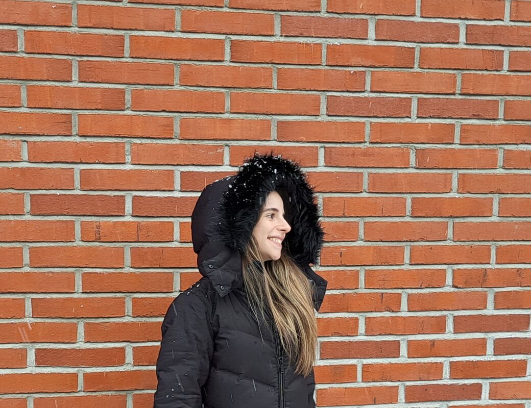Person wearing a black winter coat with fur hood stands against a red brick wall.