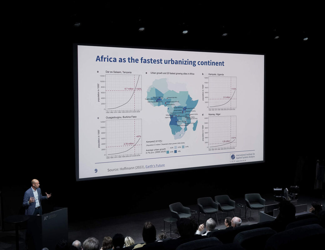 Puhuja esittelee Afrikan nopeaa kaupungistumista käsittelevää diaa hämärässä auditoriossa yleisölle.