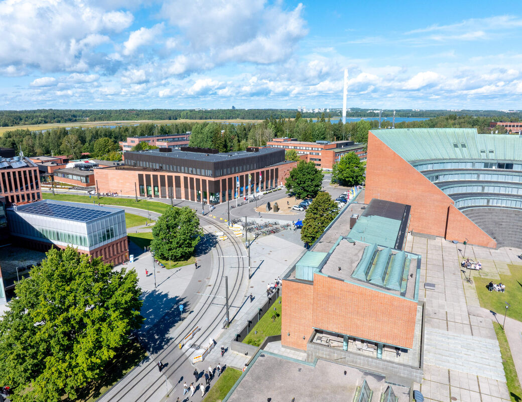 Aerial view of a modern campus with red brick buildings, tram tracks and green trees on a sunny day