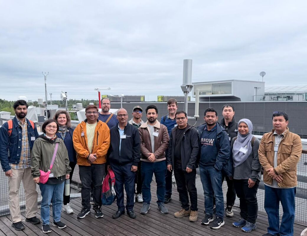 Group of people posing on a rooftop terrace with industrial buildings in the background under cloudy sky