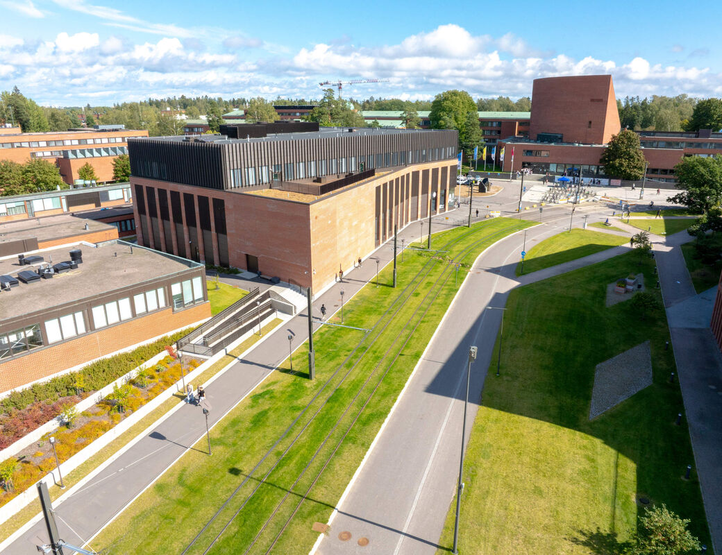 Aerial view of a modern brick campus with paths, tram tracks and green lawns on a sunny day