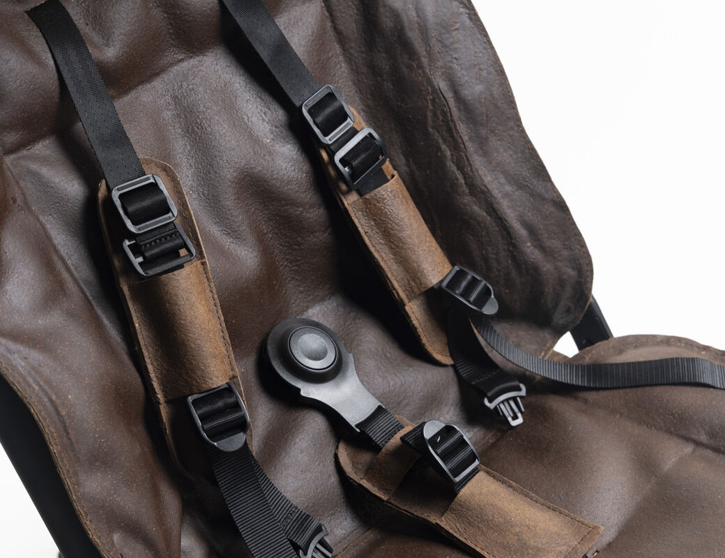 Close-up of a brown padded seat with black safety harness straps and buckles on a dark frame