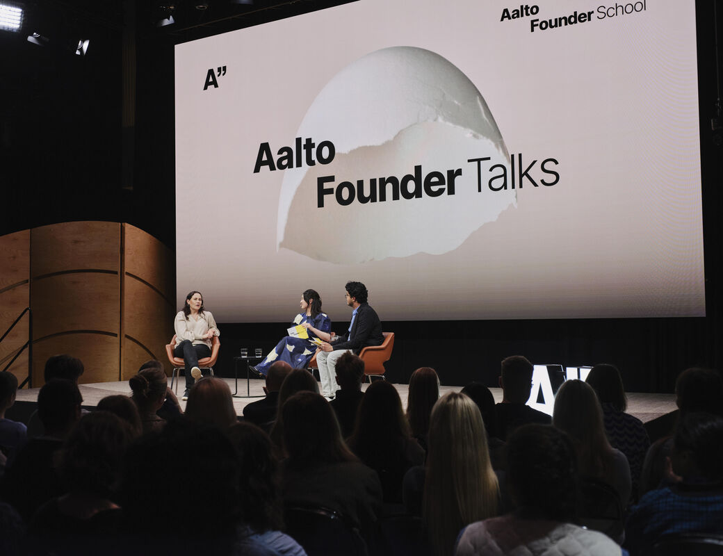 Kolme puhujaa Aalto Founder Talks -lavalla oransseilla tuoleilla, valkoinen tausta ja yleisö edessä.