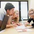 Three Aalto University students lean over a table looking at a laptop screen.