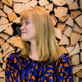 Anniina Suominen, an Associate Professor of Art Pedagogy at Aalto University’s School of Arts, Design and Architecture. She is standing in front of the camera, smiling, arms crossed. In the background there is a stack of logs.