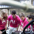 Four engineering scientists in pink t-shirts in front of an an engine