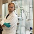 Apulaisprofessori Juha Siitonen laboratoriossa, yllään laboratoriotakki, suojalasit ja -hanskat.