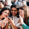Three students looking at a smartphone screen and smiling at a graduation party. Photo: Jaakko Kahilaniemi / Aalto University