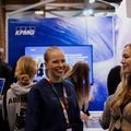 Two women smiling and standing in a crowd. Behing a blue colorful wall with TV screen and KPMG logo on it.